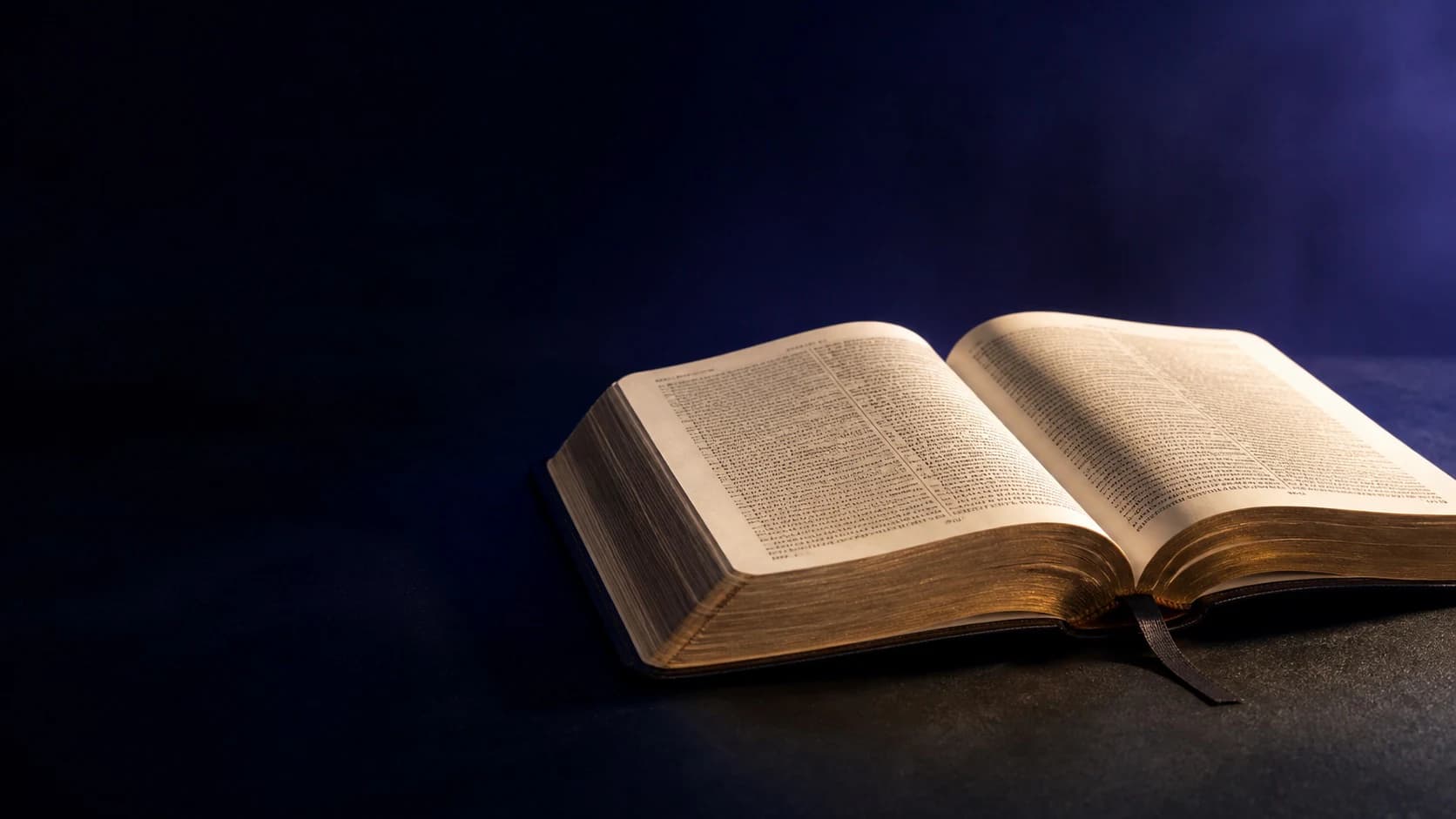 An open Bible illuminated by warm light against a deep blue and indigo background.
